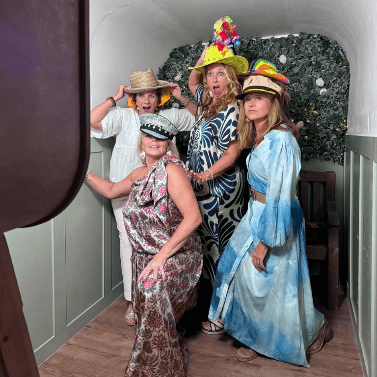 Four guests laughing and posing with hats inside the Smiles Better vintage horsebox photobooth